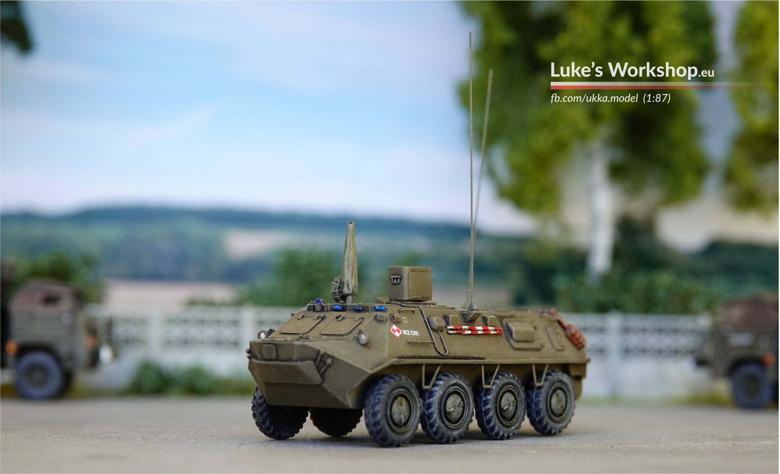BTR-60PU-12 wóz dowodzenia - widok z przodu i lewa burta. Pojazd stoi w bazie wojskowej, w tle betonowy płot oraz brzozy.
Wykonanie: Luke's Workshop